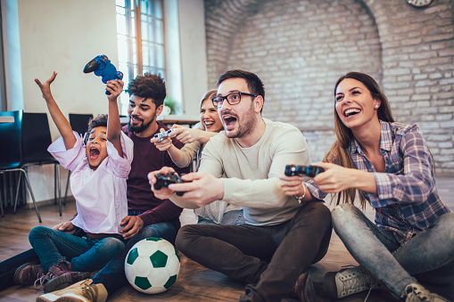 Two mixed race couple play video games with their children, having fun.