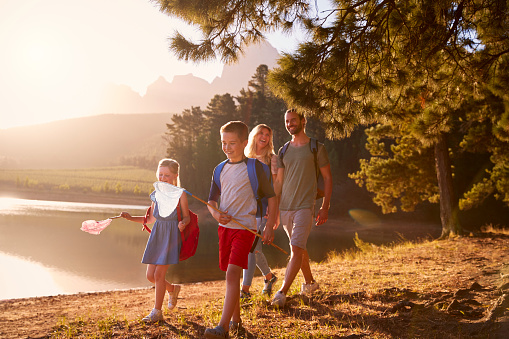 Children Walk By Lake With Parents On Family Hiking Adventure