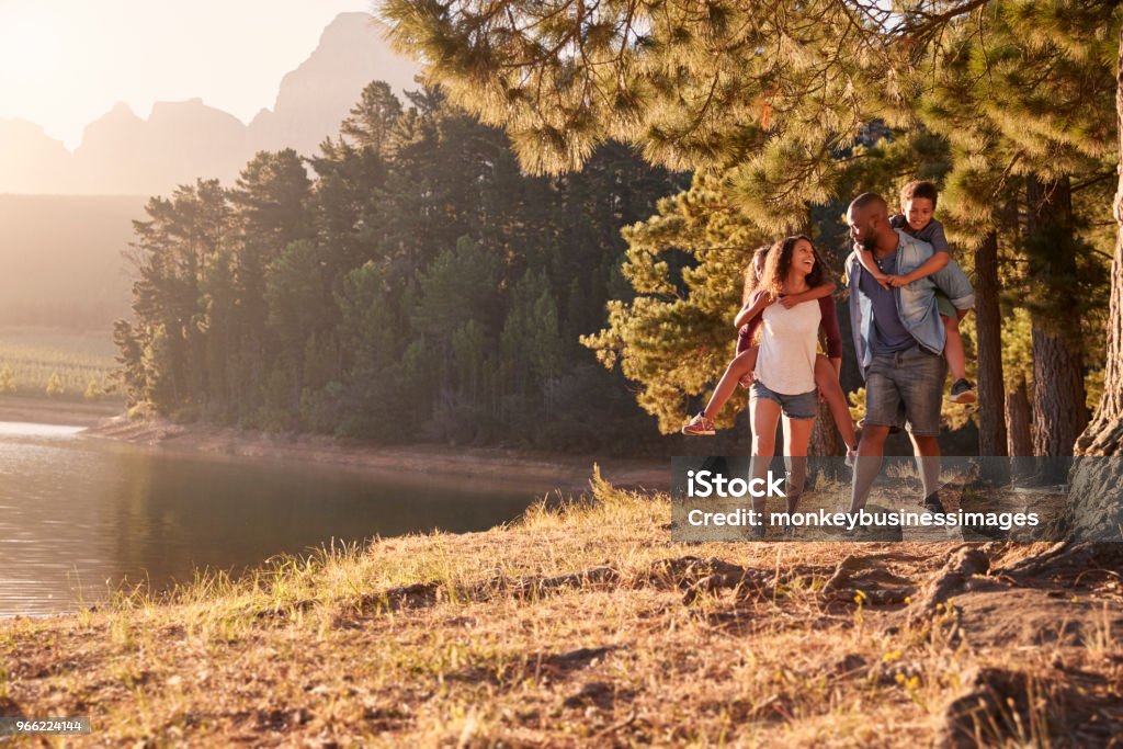 Parents Giving Children Piggyback Rides On Walk By Lake Family Stock Photo