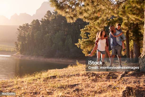 Parents Giving Children Piggyback Rides On Walk By Lake Stock Photo - Download Image Now