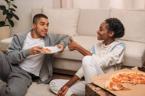 istock couple eating pizza beside sofa 966240034