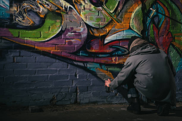 vista trasera del graffiti pintura de artista callejera con pintura en aerosol en la pared por la noche - graffiti men wall street art fotografías e imágenes de stock