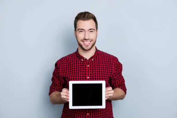 Photo of Portrait of cheerful glad confident excited professional guy showing ideal empty screen of updated upgraded tablet from brand new product line, isolated on gray background