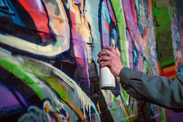 cropped view of street artist painting graffiti with aerosol paint on wall at night - graffiti men wall street art imagens e fotografias de stock