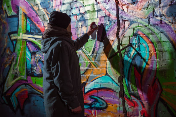street artist painting graffiti with aerosol paint on wall at night - graffiti men wall street art imagens e fotografias de stock