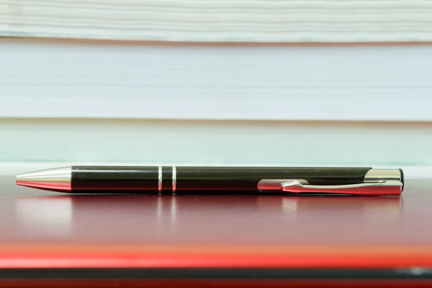 Pen on a notebook computer in front of stack of books.