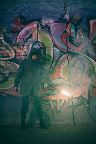 istock man holding smoke bomb and standing against wall with graffiti at night 966257166
