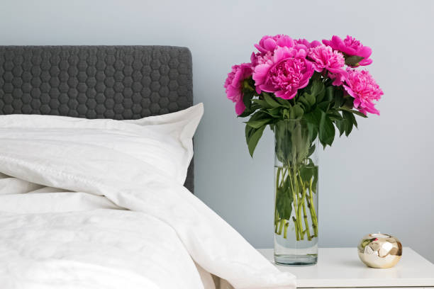 istock Bed with white bed sheets and pink peonies on the nightstand. 966262220