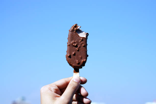 istock Hand holding chocolate ice cream bar on blue sky background. 966266722