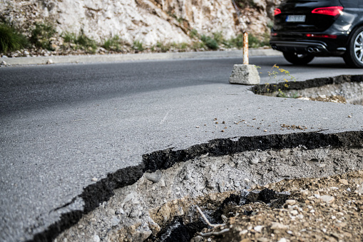 Close up view of damaged asphalt on the road with warning bars.