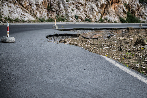 Close up view of damaged asphalt on the road with warning bars.