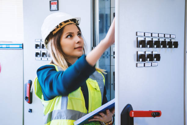 Young female maintenance engineer working at energy control room Young woman industrial service engineer wearing white helmet standing, working, checking conducts front of a control panel read and writing notes with digital tablet in energy control room of modern power plant electric energy station. XXXL size taken with Canon 5D MIV facility maintenance stock pictures, royalty-free photos & images