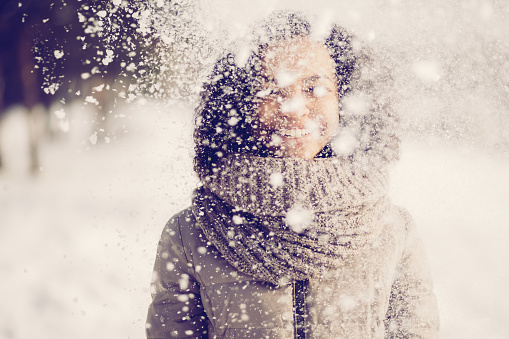 Playful young woman standing under falling snow. Carefree African woman enjoying snow and winter time. She playing with snow. Winter leisure concept