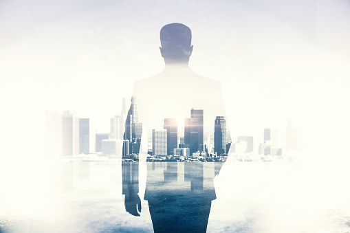 Back view of young businessman walking on abstract city background. Success and career concept. Double exposure