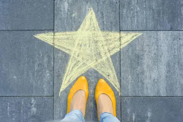 Photo of Drawing of crayons on the asphalt - star and feet of woman
