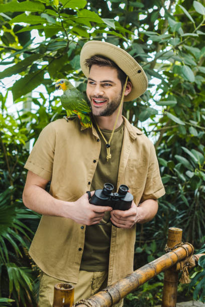 istock smiling young man with parrot on shoulder and binoculars in jungle 966346626