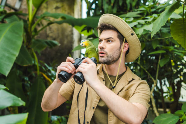 istock shocked young man with parrot on shoulder and binoculars in jungle 966346964