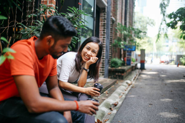 Friends chatting outdoors in Kuala Lumpur, Malaysia Young people talking and flirting on the streets of Kuala Lumpur, having a coffee break together in front of their office or university library. kuala lumpur photos stock pictures, royalty-free photos & images