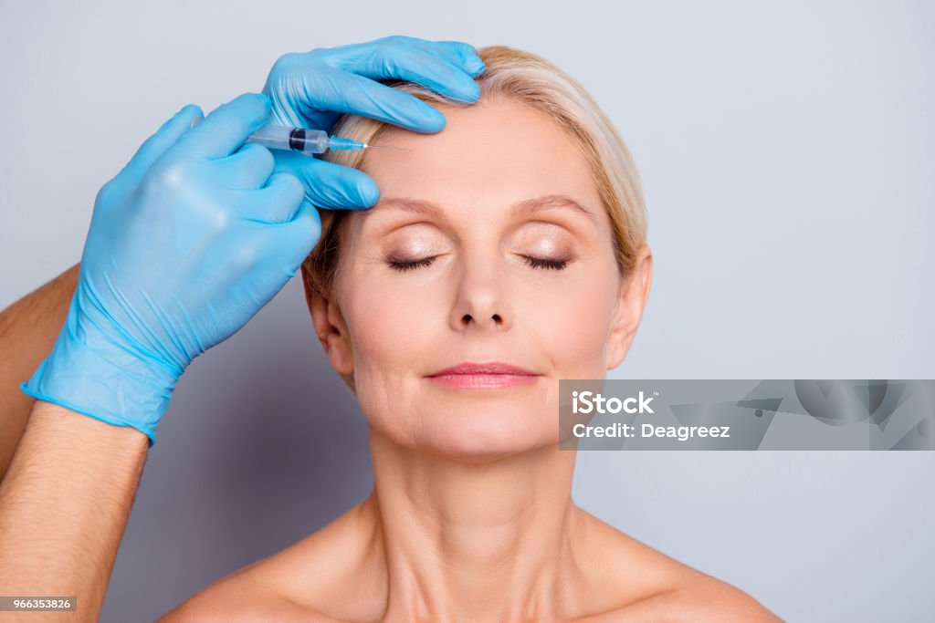 Porträt von Ernst Ruhe im Alter Frau mit Falten, die Augen schließen immer Injektion in Stirn in professionelle Klinik auf grauem Hintergrund isoliert zu halten - Lizenzfrei Botulinumtoxin-Spritze Stock-Foto