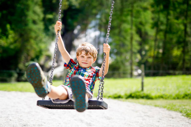 istock Funny kid boy having fun with chain swing on outdoor playground while being wet splashed with water 966364662