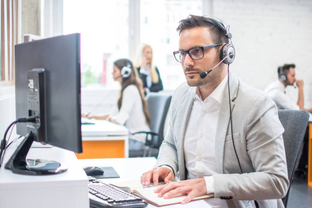 homme sérieux portant des vêtements formels et casque à la recherche à l’écran de l’ordinateur au bureau lumineux - dispatcheur photos et images de collection