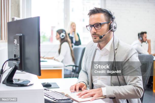 Serious Man Wearing Formal Clothes And Headset Looking At Computer Screen In Bright Office Stock Photo - Download Image Now