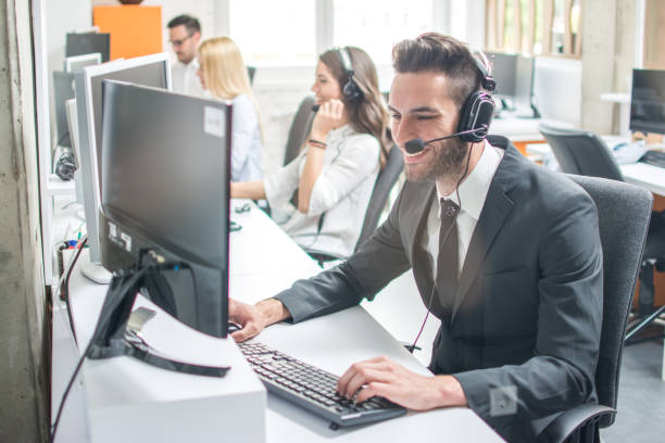 istock Smiling man in business wear with headset working on desktop computer in customer service call support helpline business center 966374478