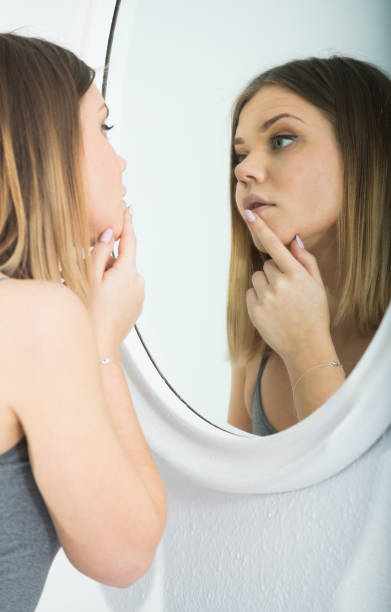 istock Young woman using mirror and touching face in bedroom 966385000