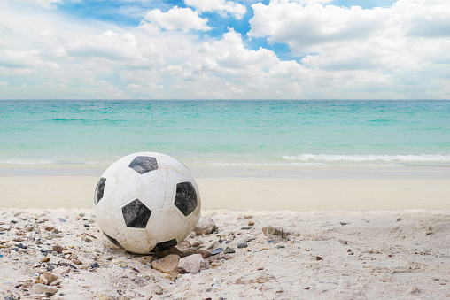 football or soccer put on the beach with blue aqua sea water and white cloud blue sky on vacation day at summer.