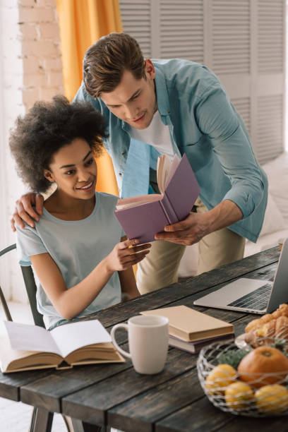 istock Multiracial boyfriend and girlfriend reading book by table at home 966430872