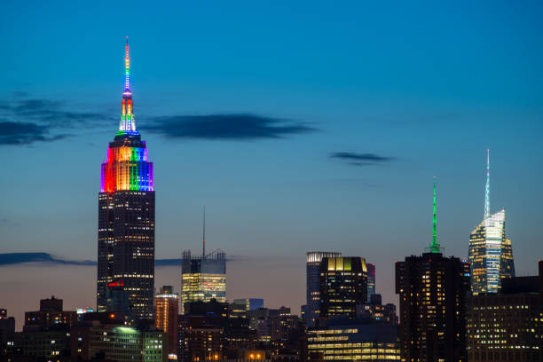 Eine teilweise Skyline von Midtown Manhattan mit dem Empire State Building, das Pride-Farben aus Brooklyn kurz vor Sonnenuntergang zeigt.