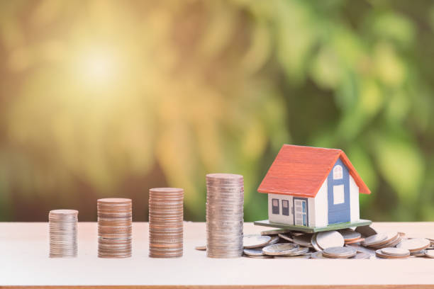 View Of coin stack with house model on green background, savings plans for housing, financial concept,Mortgage loading real estate property with loan money bank concept.Property Tax Concept stock photo