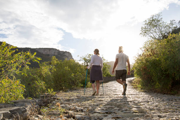 Couple ascend cobblestone path at sunrise Woman uses hiking poles and knee brace for support knee brace stock pictures, royalty-free photos & images