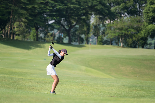 An Asian woman hits the perfect golf shot from the fairway towards the putting green