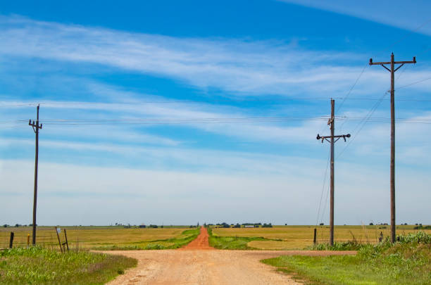 la route moins parcourue - une croix rurale routes avec un chemin de terre rouge pointe vers l’avant au-dessus de l’horizon en pays ferme sous ciel très bleu - oklahoma agriculture landscape nature photos et images de collection