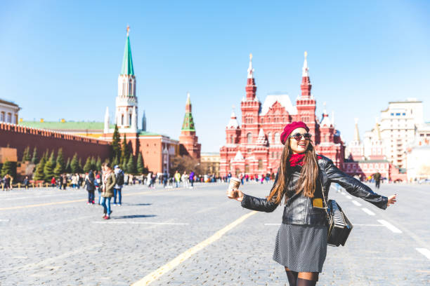 Happy beautiful woman in Moscow Red Square, with Kremlin and museum buildings on background. Vintage looking girl wearing sunglasses and wool hat, tourist in Moscow, Russia. Travel, lifestyle concepts