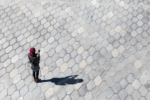 Woman typing on the phone, shadow and empty space. Minimal image, top view of a girl with a smartphone, and her shadow on the pavement. Technology concept, blank space to add text.
