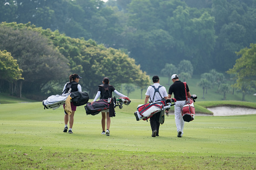 A group of friends talk to each other as they walk with their golf bags down the fairway