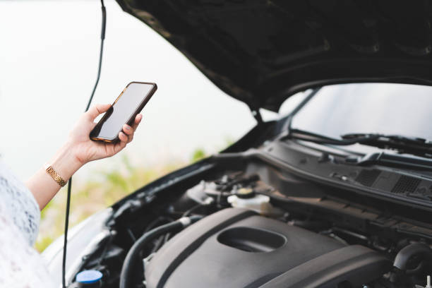 istock Woman hand using mobile phone with a broken car to call assistance on roadside. 966489658