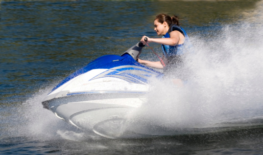 Close-up side view action photo of a young woman on a sporty Seadoo watercraft with water spray 