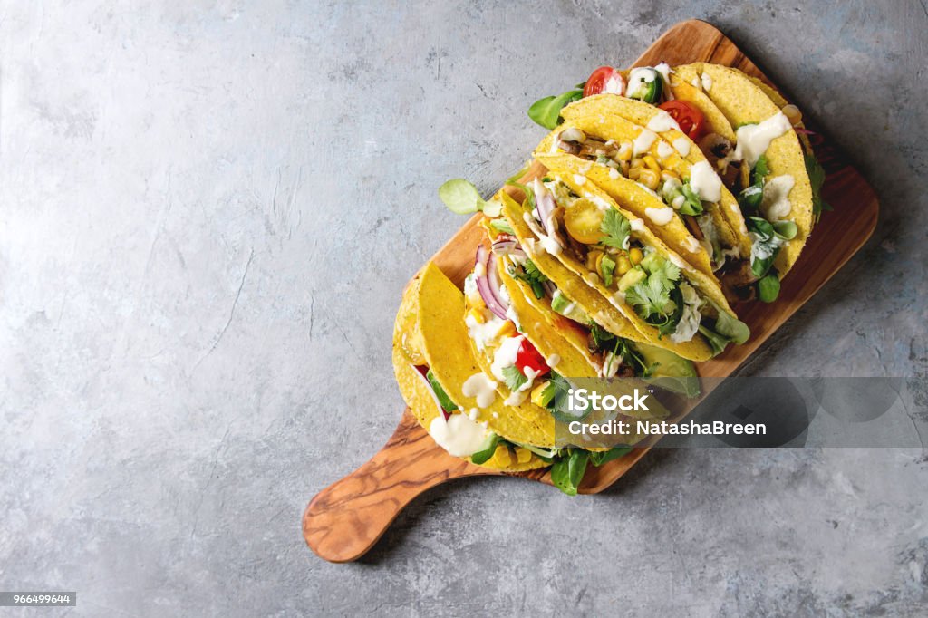 Vegetarian corn tacos Variety of vegetarian corn tacos with vegetables, green salad, chili pepper served on olive wood board with cream sauce over grey texture background. Top view, copy space. Taco Stock Photo