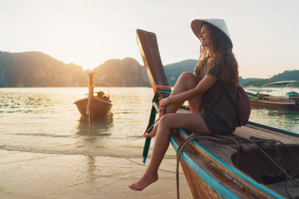 Breathtaking Destinations Beautiful caucasian woman with an asian style conical hat sitting on a longtail boat and enjoying a carefree summer day on the beach. explorer photos stock pictures, royalty-free photos & images