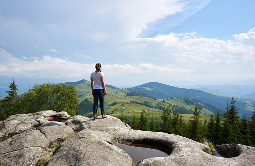 A teenage hiker with poles and a backpack while wandering to the top of Mount Nanos in Slovenia. At the top, a beautiful view of the valley.  He stands triumphantly on the edge of the ridge and screams with raised hands.
