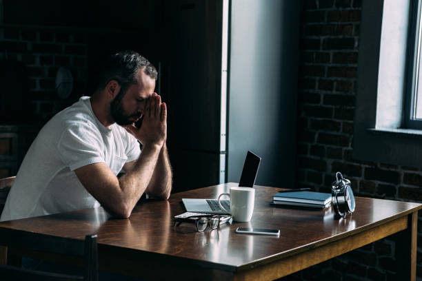 istock depressed young man sitting on kitchen with laptop and leaning head on hands 966526962