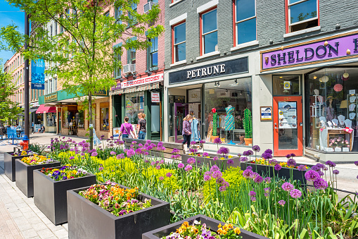 People walk past colorful stores in a pedestrian area of downtown Ithaca, New York State, USA on a sunny day.