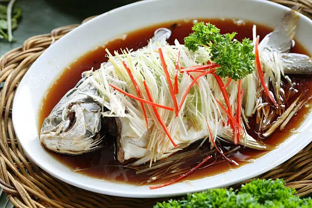 Photo of Steamed fish covered in vegetables in a brown liquid