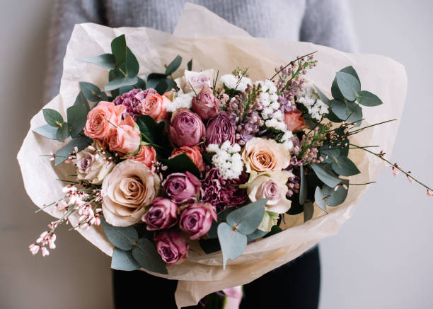 giovane donna fioraio che tiene un bouquet di fiori in fiore appena fatto di rose ed eucalipto sullo sfondo grigio della parete. - rose pink flower valentines day foto e immagini stock