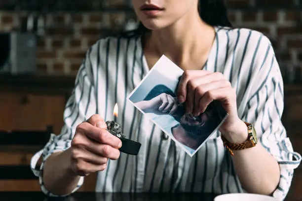 cropped shot of young woman burning photo card of ex-boyfriend