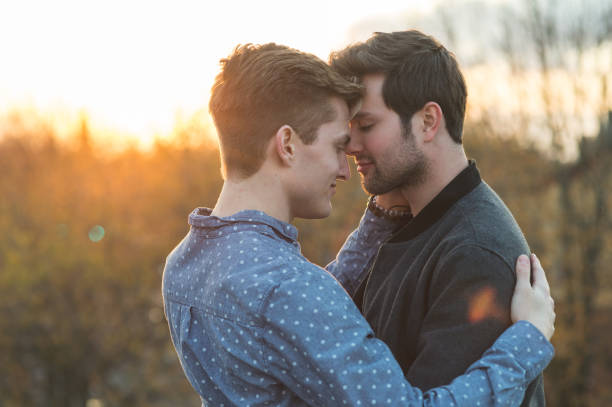 jeune couple mâle gay profiter d’un beau coucher de soleil à l’extérieur ensemble - gay man homosexual sex men photos et images de collection