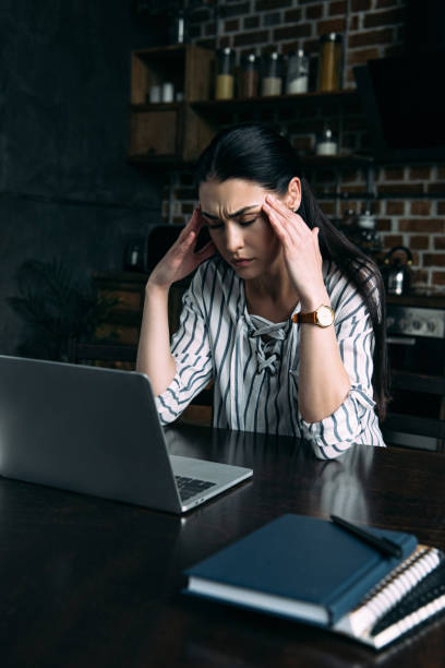 istock stressed young woman with headache sitting on kitchen with laptop 966561706
